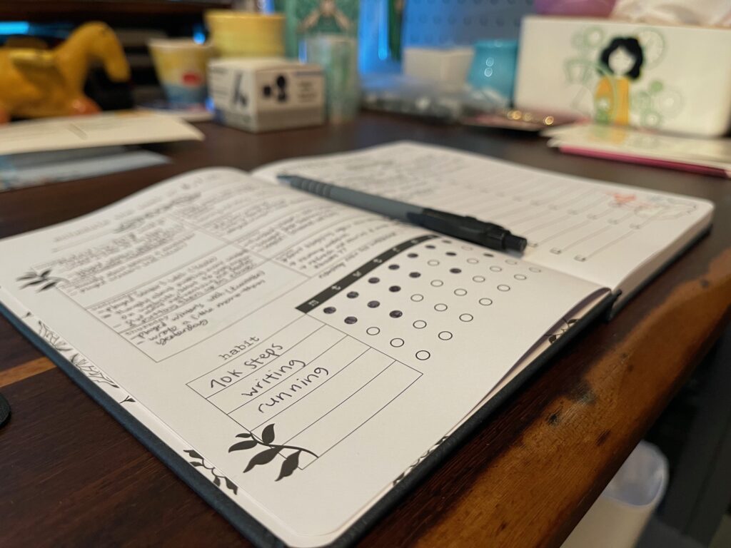 A weekly planner open on a table showing some daily habits filled in: 10k steps, writing, running.